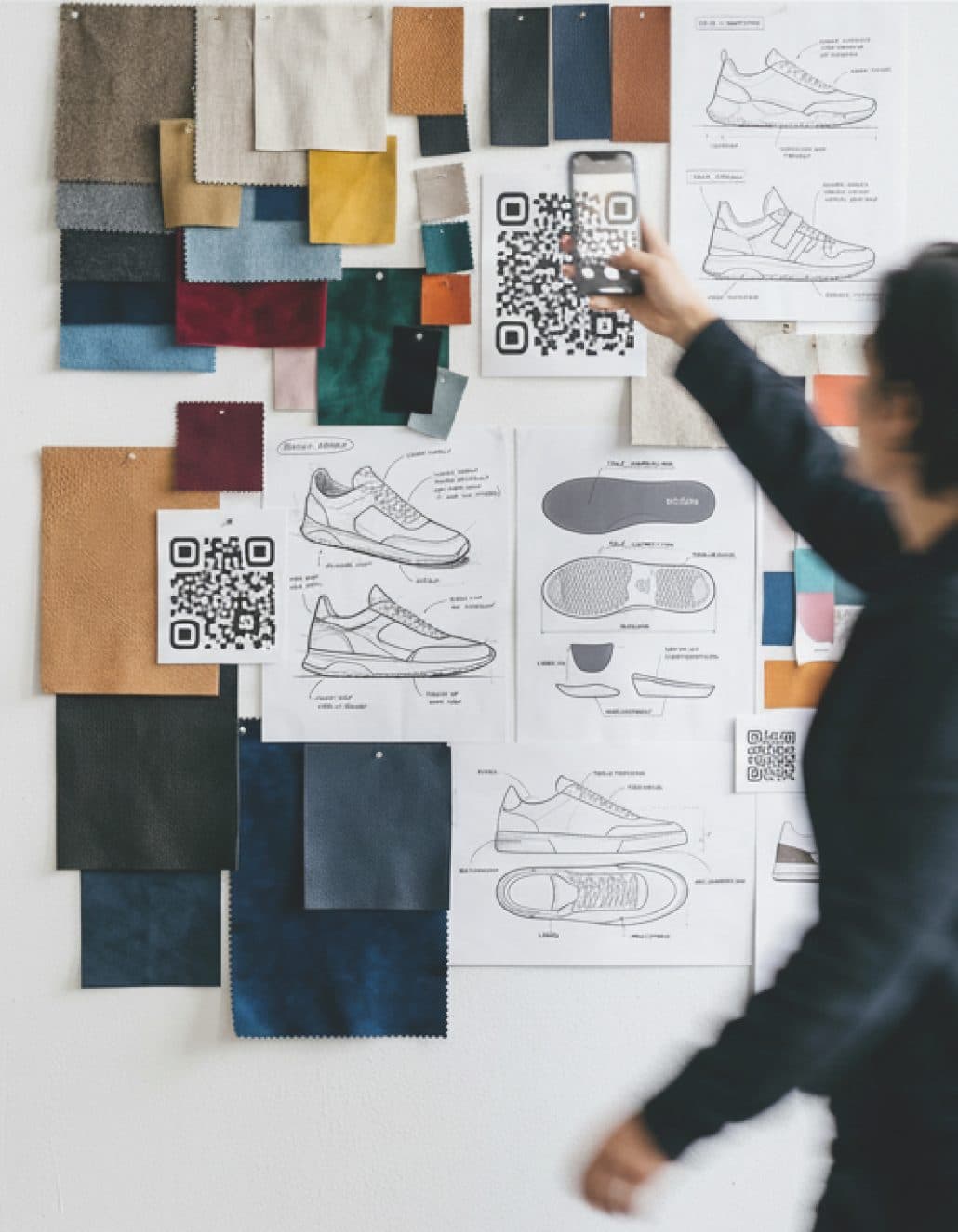 A designer scanning QR-coded fabric swatches and product sketches on a studio wall